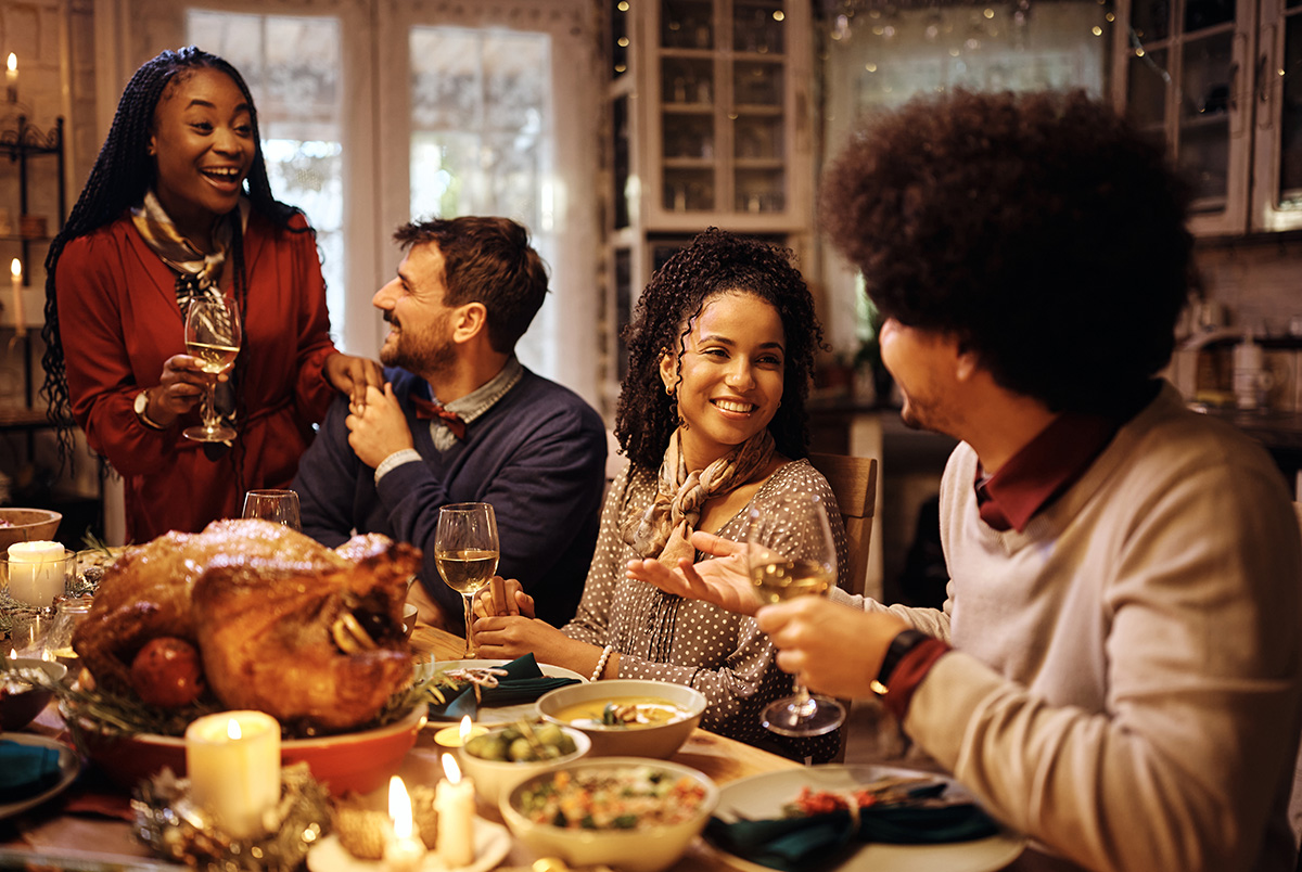 A woman holding a glass of wine at a Thanksgiving table with turkey, friends, and family as part of our holiday party safety tips.