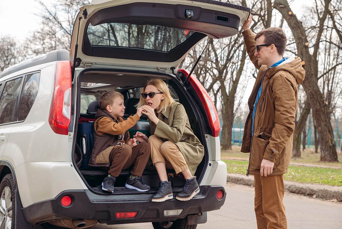 A family sitting/standing at the back of a white SUV as part of our Thanksgiving travel tips for safe driving.