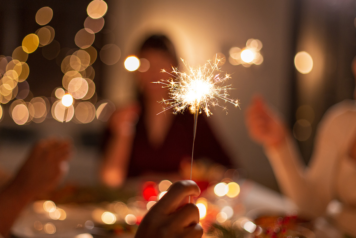 A sparkler with a NYE party in the background for common causes of NYE party slip and falls.