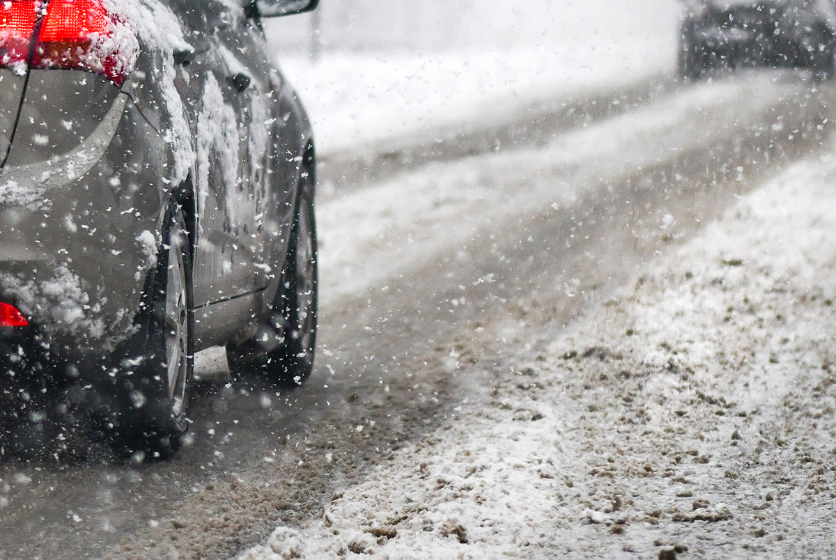 A car driving down a snowy road for our post on winter driving safety tips.