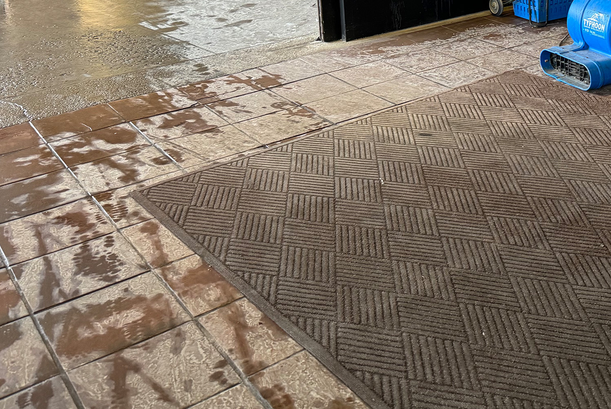 A brown entrance mat on a wet brown tile floor to demonstrate slip and fall prevention.