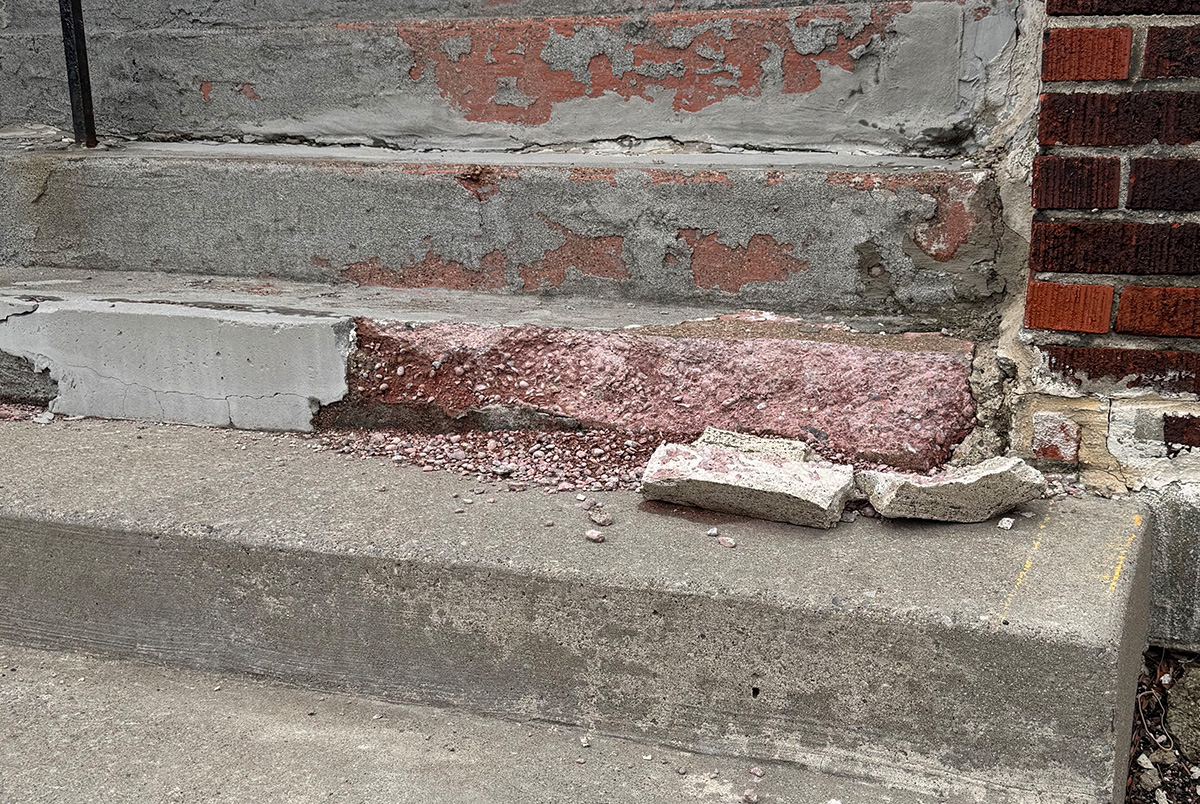 A missing step where the concrete is half deteriorated and crumbled on the step below, creating a safety hazard.