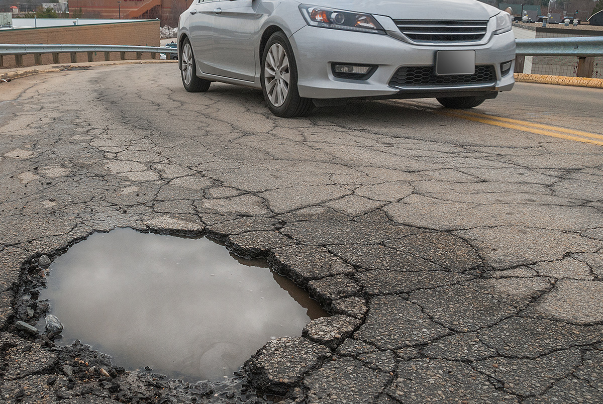 A silver car crossing a double yellow line to avoid a pothole full of water to illustrate the dangers of swerving.