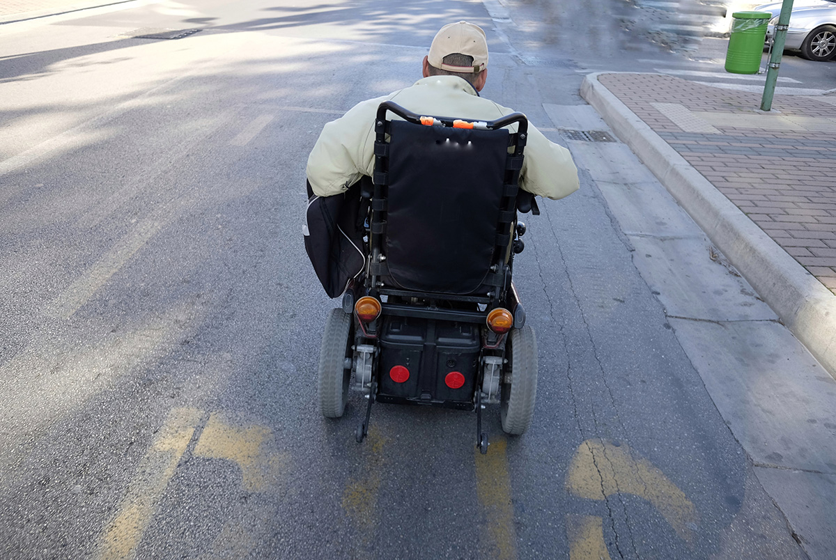 A man in an electric wheelchair riding in the street. Districted driving puts pedestrians like this at risk.