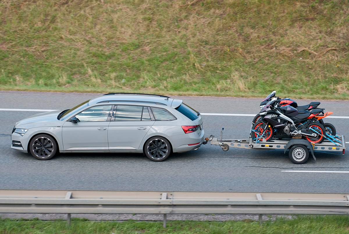 A silver hatchback towing a trailer with motorcycles down a highway to illustrate safe towing.