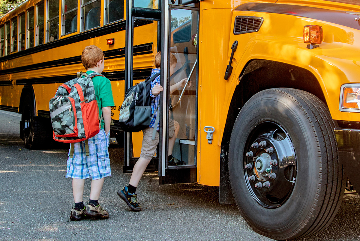 Two little boys boarding a school bus to illustrate important back to school dates.