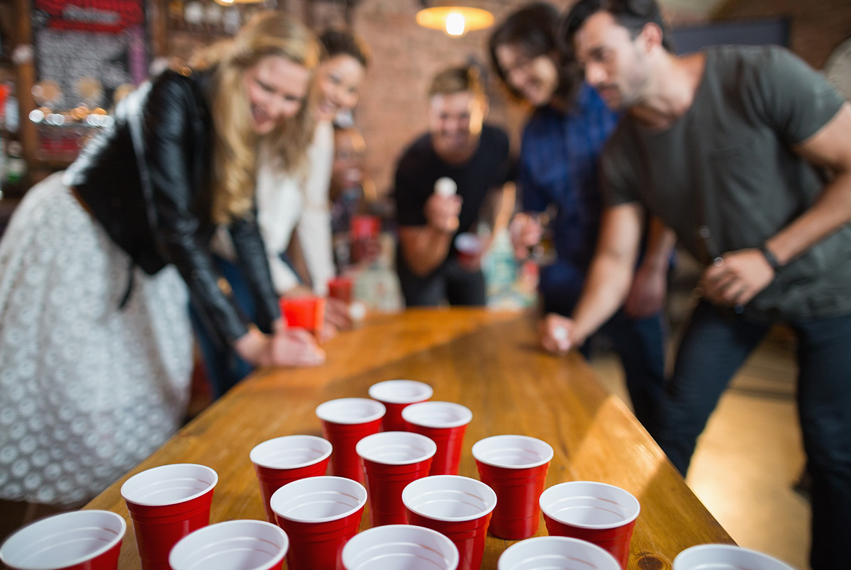 A out of focus group of friends playing beer pong where the cups are in focus to illustrate Labor Day being one of the top ten booziest holidays.