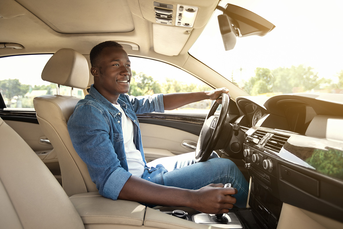 A black man in a jean jacket driving inside a light colored car interior to advertise the importance of Supplemental Underinsured Motorist Coverage.